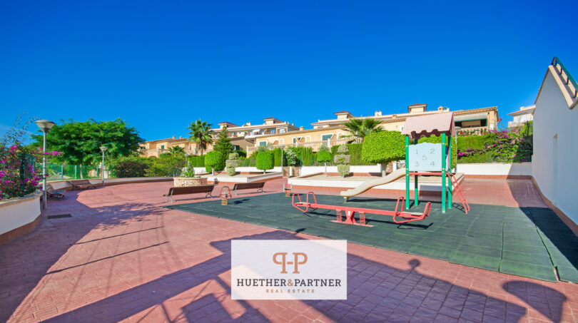 Gemeinschaftsbereich der Wohnanlage in Cales de Mallorca mit Kinderspielplatz, Sitzbänken und gepflegten Grünanlagen.