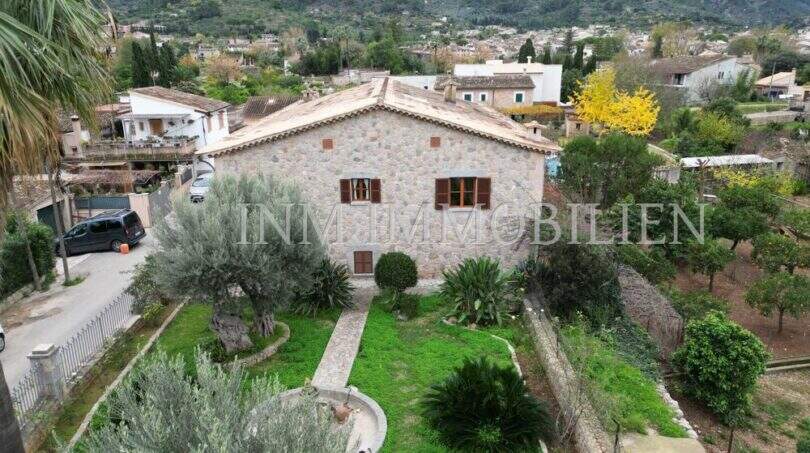 Vista aérea de una finca rústica de piedra natural en Sóller con jardín cuidado, olivos y panorama montañoso.