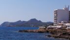 Küstenblick in Cala Ratjada: Felsige Meeresküste mit Hotelgebäude und Bergen im Hintergrund, Mallorca.