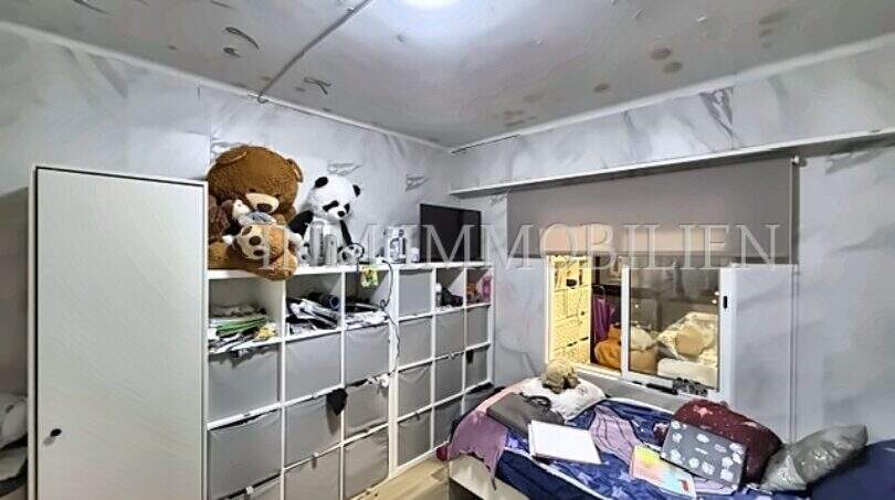 Kinderzimmer mit Einzelbett, weißem Regalschrank, Teddybären und Marmoroptik-Tapete in Strandnähe-Wohnung.