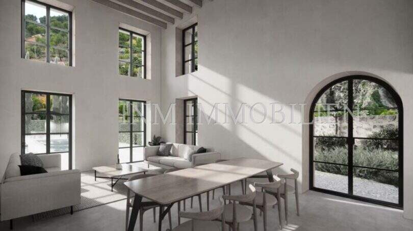 Zona de estar luminosa con techo alto, ventanas de arco de medio punto y vista al jardín mediterráneo de la finca en Sóller.