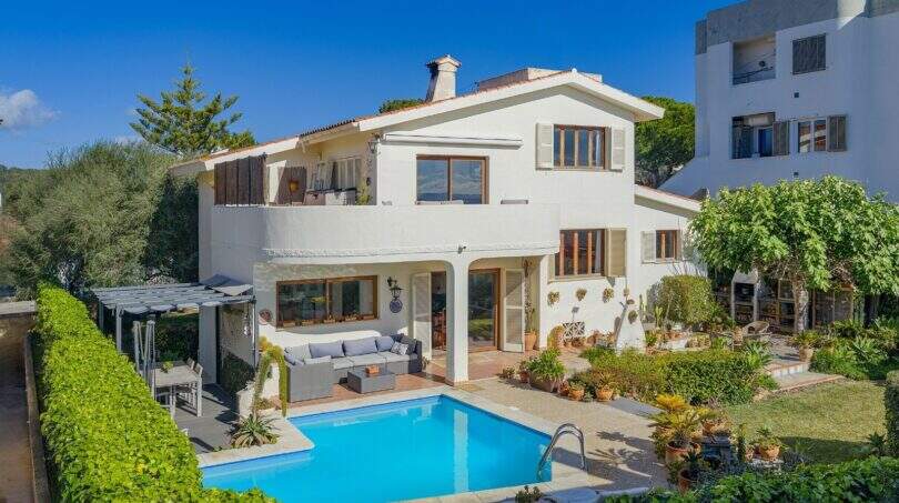 Villa mediterránea en Alcanada con piscina, área lounge, balcón y jardín exuberante bajo cielo azul.