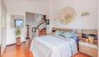 Dormitorio luminoso de villa mediterránea con suelo de terracota, cama doble, escaleras y espejo con vista al mar