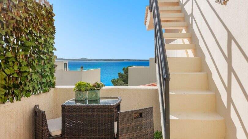 Terraza con muebles de ratán, escaleras y vista al mar azul turquesa de villa mediterránea en Alcanada