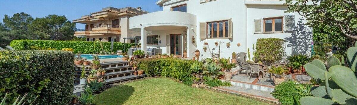 Vista exterior de villa mediterránea Alcanada: casa blanca, jardín cuidado, piscina y terraza con área de estar.