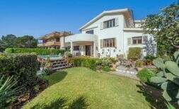 Exterior view Mediterranean villa Alcanada: white house, well-maintained garden, swimming pool and terrace with seating area.