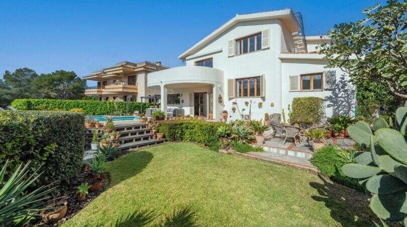 Vista exterior de villa mediterránea Alcanada: casa blanca, jardín cuidado, piscina y terraza con área de estar.