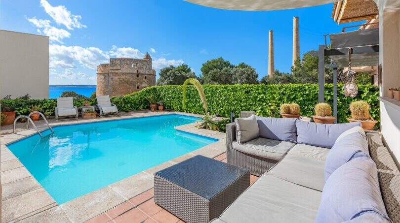 Área exterior de villa mediterránea en Alcúdia con piscina, muebles lounge, torre de vigilancia histórica y vista al mar