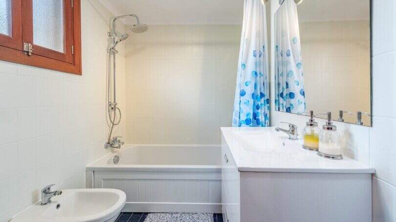 Baño luminoso de villa mediterránea en Alcanada con bañera, ducha de lluvia y cortina de ducha azul.