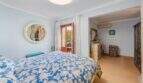 Dormitorio luminoso de villa mediterránea en Alcanada con cama doble, espejo redondo y acceso a balcón