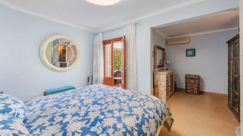Dormitorio luminoso de villa mediterránea en Alcanada con cama doble, espejo redondo y acceso a balcón