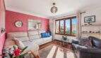 Sala de estar luminosa de villa mediterránea en Alcúdia con pared de acento rojo, sofás y vista al mar a través de la ventana.