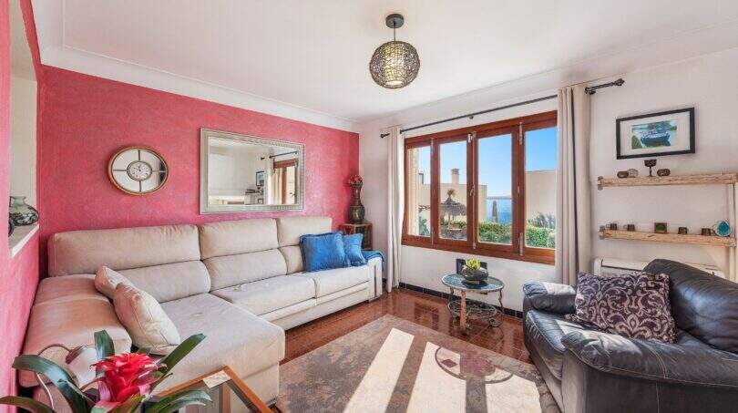 Sala de estar luminosa de villa mediterránea en Alcúdia con pared de acento rojo, sofás y vista al mar a través de la ventana.