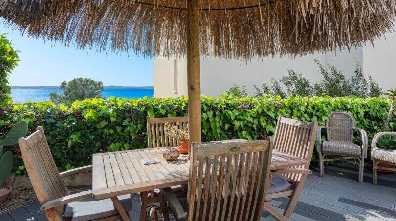 Terraza soleada con muebles de madera, techo de paja y vista al mar de villa mediterránea en Alcanada