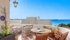 Terraza soleada con muebles de ratán, mesa de madera y vista al mar al azul turquesa del Mediterráneo en Alcanada