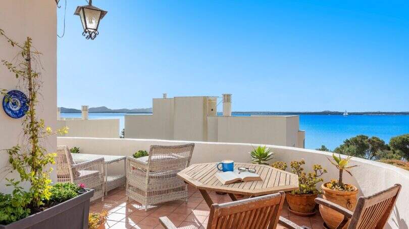 Terraza soleada con muebles de ratán, mesa de madera y vista al mar al azul turquesa del Mediterráneo en Alcanada