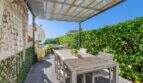 Terraza cubierta con mesa de madera, vista al mar y área de piscina de villa mediterránea en Alcanada