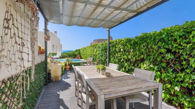 Terraza cubierta con mesa de madera, vista al mar y área de piscina de villa mediterránea en Alcanada
