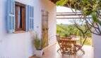 Covered terrace of the finca with wooden furniture, blue shutters and view into the green hinterland