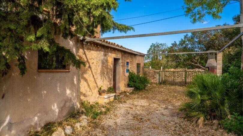 Rustic stone building of the finca from 1890 with wooden door, gravel floor and Mediterranean planting.