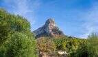 View of the distinctive rock peak with lush vegetation and traditional country house of the historic finca in Colònia de Sant Pere