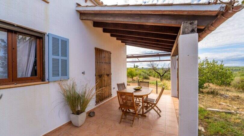 Covered terrace of the finca with wooden beams, dining table and view of the landscape of Colònia de Sant Pere