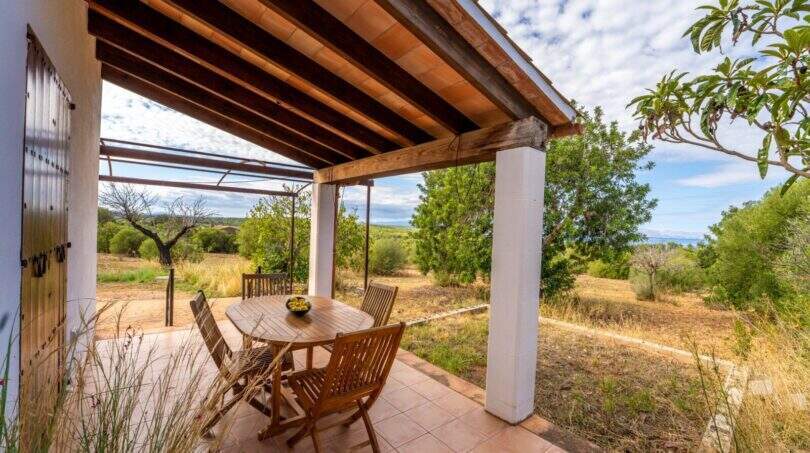 Covered terrace of the finca with wooden beams, dining table and view of nature and sea in Colònia de Sant Pere