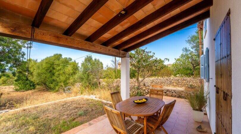Covered terrace of the finca with wooden beams, seating group and view of the natural garden.