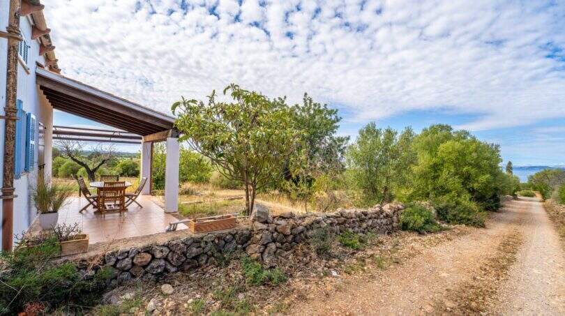Covered terrace of the finca with stone wall, gravel path and view of Mediterranean garden and sea view