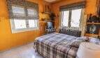 Schlafzimmer der Villa in Marratxí mit orangefarbenen Wänden, Doppelbett und Zebra-Jalousien an zwei Fenstern.