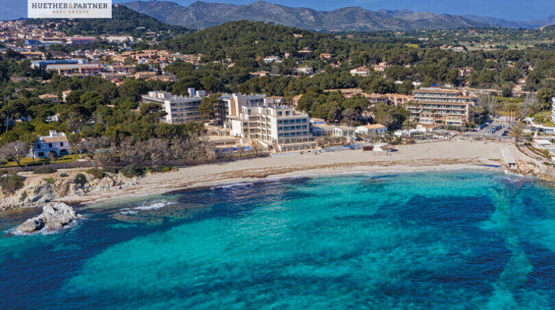 Luftaufnahme einer Neubauwohnung direkt am türkisblauen Strand von Cala Ratjada mit Bergpanorama.