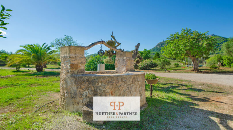 Fuente de piedra rústica en la finca de Felanitx con jardín verde y vistas a la montaña en Sant Salvador