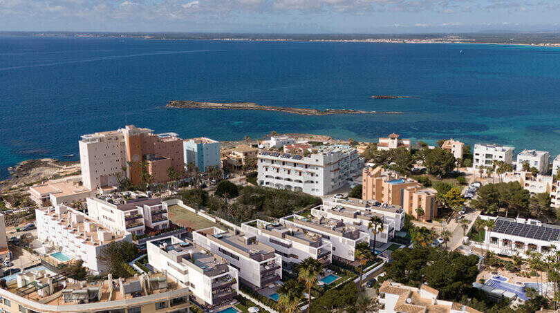 Luftaufnahme von Colonia de Sant Jordi mit weißen Apartments, Palmen und türkisblauem Mittelmeer im Hintergrund.