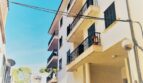 Außenansicht eines weißen Mehrfamilienhauses mit Balkonen in Cala Ratjada, Mallorca, direkt am Hafen gelegen.
