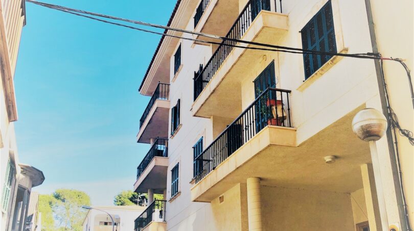 Außenansicht eines weißen Mehrfamilienhauses mit Balkonen in Cala Ratjada, Mallorca, direkt am Hafen gelegen.