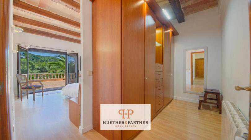 Área de vestidor con armario empotrado de madera, techo de vigas de madera y vistas al dormitorio luminoso con vistas a la montaña.