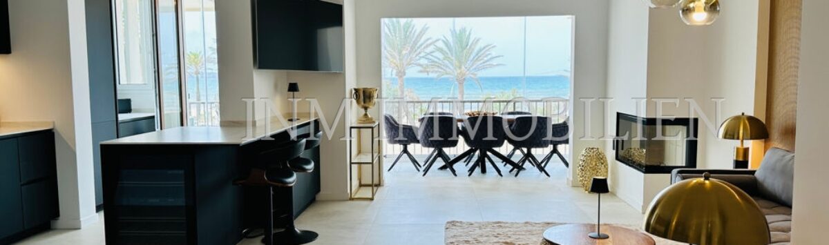 Open living-dining area with sea view, dark kitchen island, gold accents and designer lamps in Palma de Mallorca