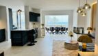 Open living-dining area with sea view, dark kitchen island, gold accents and designer lamps in Palma de Mallorca