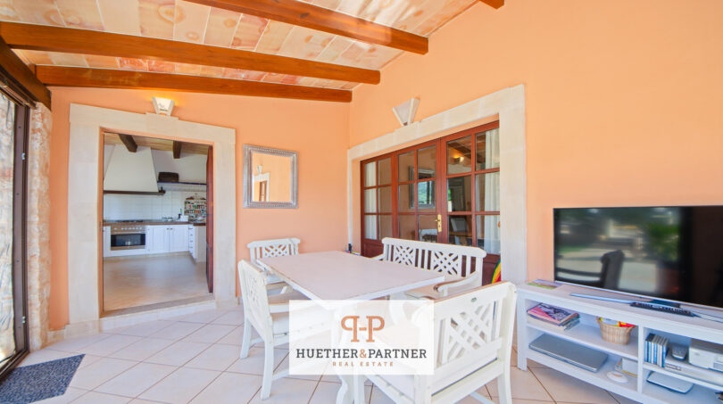 Comedor luminoso de la finca Felanitx con techo de vigas de madera, muebles blancos y vistas a la cocina