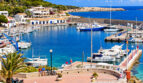 Hafen von Cala Ratjada mit Booten, blauem Wasser, weißen Gebäuden und Promenade auf Mallorca