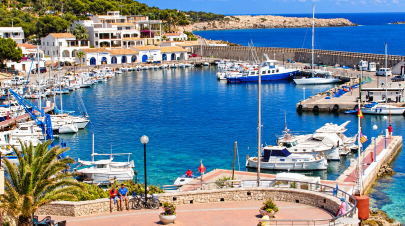 Hafen von Cala Ratjada mit Booten, blauem Wasser, weißen Gebäuden und Promenade auf Mallorca