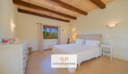 Dormitorio luminoso de la finca Felanitx con techo de vigas de madera, cama doble y suelo de piedra natural