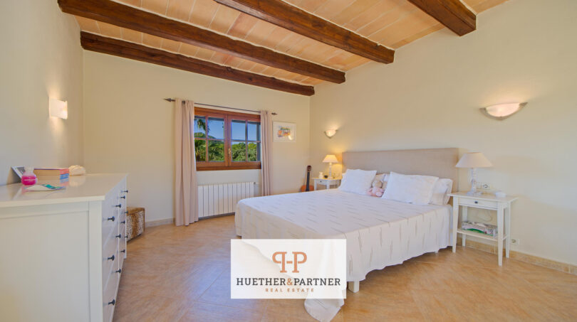 Dormitorio luminoso de la finca Felanitx con techo de vigas de madera, cama doble y suelo de piedra natural