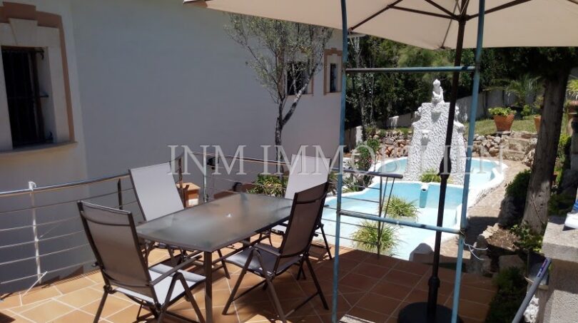 Terraza soleada con muebles de jardín y sombrilla, vista de la piscina y escultura, casa unifamiliar Santa Ponsa