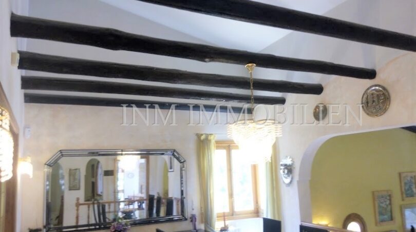 Sala de estar con vigas de madera negra rústicas, techo abovedado y elegante lámpara de araña en villa Santa Ponsa