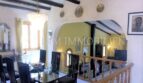 Área de estar-comedor abierta con vigas de madera en el techo, mesa de cristal y barandilla de escalera en Villa Santa Ponsa