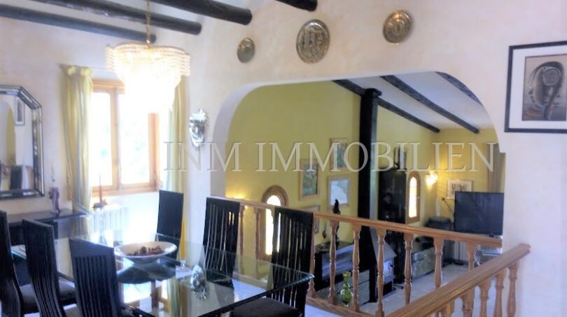 Área de estar-comedor abierta con vigas de madera en el techo, mesa de cristal y barandilla de escalera en Villa Santa Ponsa