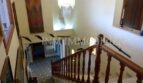 Elegante escalera con barandilla de madera, lámpara de araña y tapiz de pared en casa unifamiliar Santa Ponsa