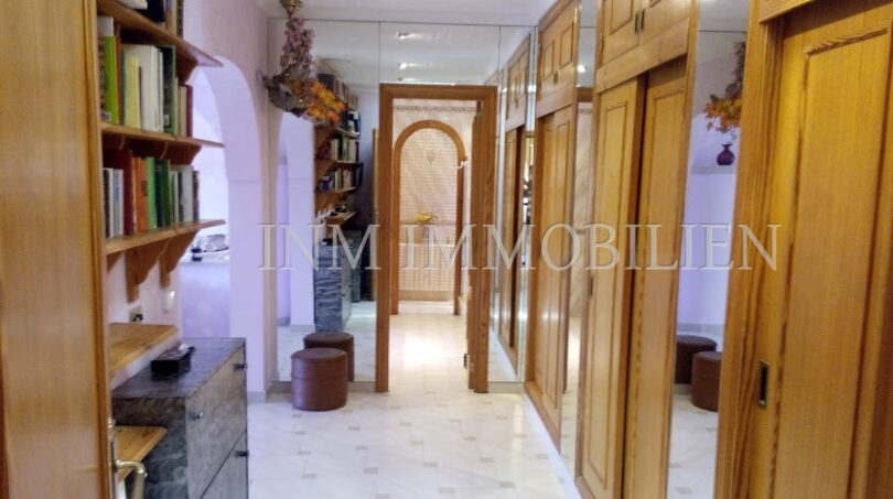 Pasillo luminoso con armarios empotrados de madera, pared de espejo y estantería en casa unifamiliar Santa Ponsa