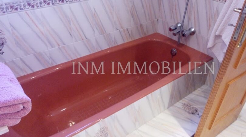 Baño con bañera empotrada roja, baldosas de mármol y puerta de madera en casa unifamiliar Santa Ponsa